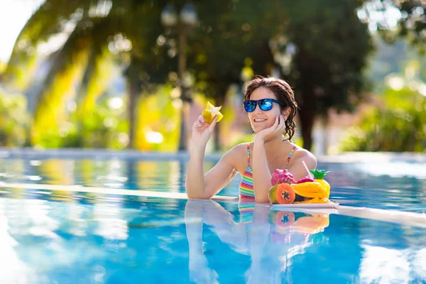 Tropical fruit plate at swimming pool. Young woman eating mango, pineapple, orange and drinking fresh juice on summer vacation at exotic island. Healthy nutrition. Beach holiday and swim fun.