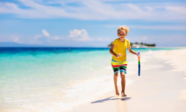 Child surfing on tropical beach. Family summer vacation in Asia. Kids swim in ocean water. Kid on surf body board. Little boy swimming in exotic sea. Travel with children. Water and beach sport.