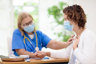 Doktor maske takan hasta hastayı muayene ediyor. Test ve tarama için sağlık kliniğindeki hasta kadın. Evde virüs tedavisi. Koronavirüs salgını. Covid-19 salgını. Kadın öksürüyor, göğsü ağrıyor..