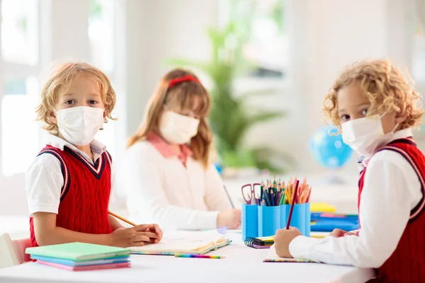 Kids in face mask in school class. Child back to school after coronavirus lockdown. Primary child in covid-19 pandemic. Safety and virus spread prevention. Student in surgical mask. Social distancing.