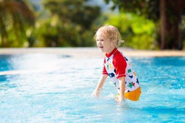 Çocuk havuzda oynuyor. Çocuklarla yaz tatili. Tropik bir adada egzotik tatilde suya atlayan küçük bir çocuk. Çocuklar yüzer. Anaokulu öncesi için aktif açık hava sporu.