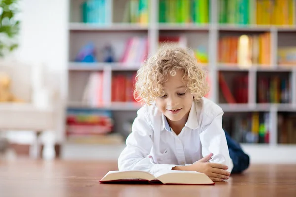 孩子们看书 孩子们读书 一个小男孩在一个五颜六色的书架上为学校做作业 学生与书籍 108 早期教育和发展 儿童之家图书馆 学龄前儿童学习 — 图库照片