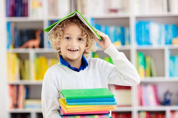 孩子们看书 孩子们读书 一个小男孩在一个五颜六色的书架上为学校做作业 学生与书籍 108 早期教育和发展 儿童之家图书馆 学龄前儿童学习 — 图库照片