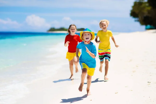 熱帯のビーチで遊んでいる子供たち 子供たちは夏休みに海で泳いだり遊んだりします 砂と水の楽しさ 太陽の保護 海の岸を走って飛び跳ねる小さな子供 — ストック写真