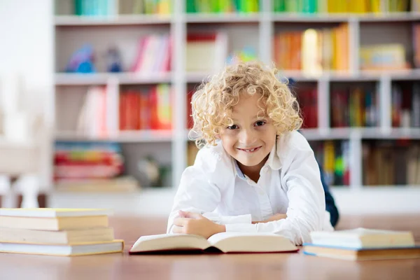孩子们看书 孩子们读书 一个小男孩在一个五颜六色的书架上为学校做作业 学生与书籍 108 早期教育和发展 儿童之家图书馆 学龄前儿童学习 — 图库照片