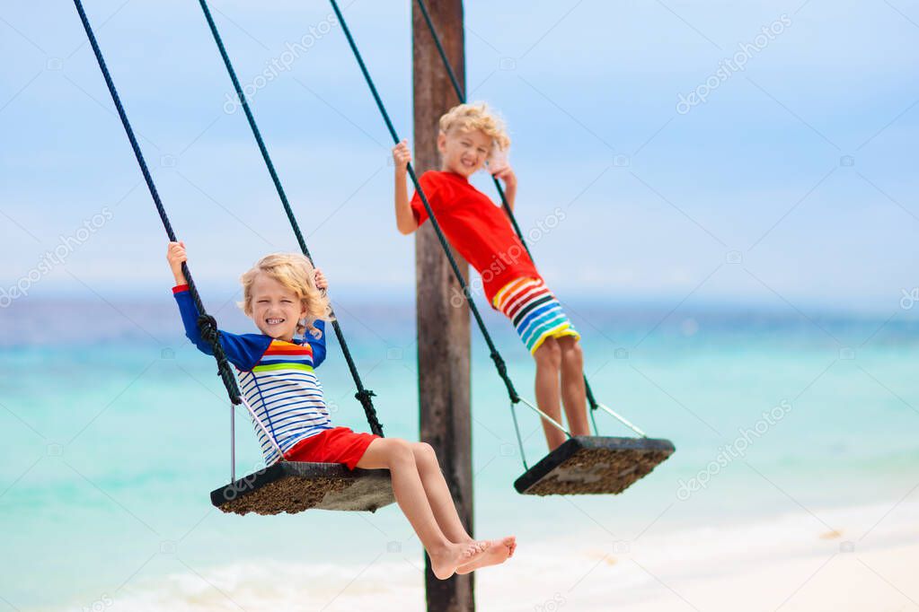 Child on beach swing. Kid swinging on tropical island. Travel with young children. Summer family exotic vacation. Kids play on sea shore. Little girl and boy playing in luxury ocean resort.