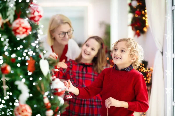 Child decorating Christmas tree at home. Little boy and girl with Xmas ornament. Family with kids celebrate winter holidays. Mother and kids decorate living room and fireplace for Christmas.