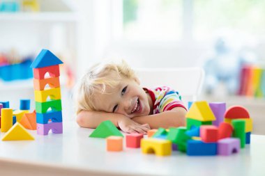 Çocuk renkli oyuncak bloklarıyla oynuyor. Küçük çocuk oyuncaklardan kule inşa ediyor. Küçük çocuklar için eğitici ve yaratıcı oyuncaklar ve oyunlar. Gökkuşağı tuğlalı beyaz yatak odasındaki bebek. Evdeki çocuk.