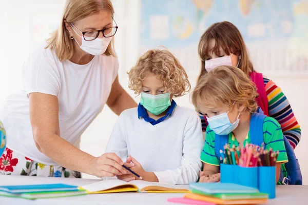 Teacher in class, school child in face mask during corona virus and flu outbreak. Boy and girl back to school after covid-19 quarantine and lockdown. Group of kids in masks for coronavirus prevention.