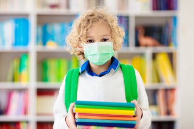Corona virüsü ve grip salgını sırasında yüz maskesi takan okul çocuğu. Çocuk karantina ve tecritten sonra okula geri dönüyor. Koronavirüsü önlemek için maskeli çocuklar kütüphanede.. 