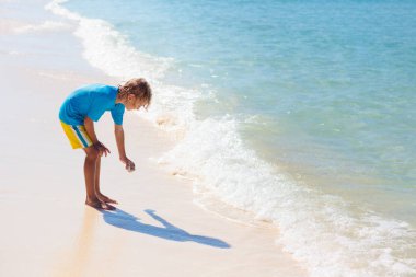 Tropik plajda oynayan çocuklar. Çocuklar yaz tatilinde yüzer ve denizde oynarlar. Kum ve su eğlencesi, küçük çocuklar için güneş koruması. Okyanus kıyısında koşan ve zıplayan küçük çocuk.