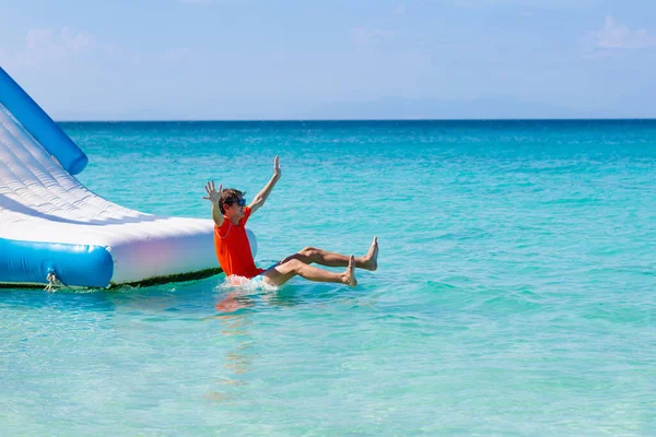 熱帯の海のビーチでトランポリンでジャンプする子供たち 子供たちは膨脹可能なウォータースライドでジャンプします エキゾチックな島のリゾートでアクアアミューズメントパーク 家族での休暇と子供との旅行 海沿岸の楽しみ — ストック写真