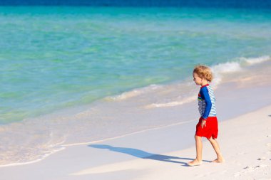 Tropik plajda oynayan çocuklar. Çocuklar yaz tatilinde yüzer ve denizde oynarlar. Kum ve su eğlencesi, küçük çocuklar için güneş koruması. Küçük çocuk ve kız okyanus kıyısında koşup zıplıyorlar..