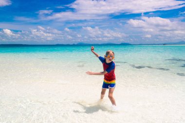 Tropik plajda oynayan çocuklar. Çocuklar yaz tatilinde yüzer ve denizde oynarlar. Kum ve su eğlencesi, küçük çocuklar için güneş koruması. Okyanus kıyısında koşan ve zıplayan küçük çocuk.