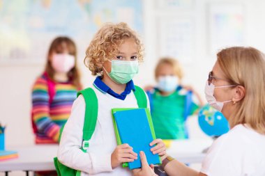 Sınıfta öğretmen, Corona virüsü ve grip salgını sırasında maskeli okul çocuğu. Erkek ve kız covid-19 karantina ve tecritten sonra okula dönüyorlar. Koronavirüsü önlemek için maskeli bir grup çocuk..