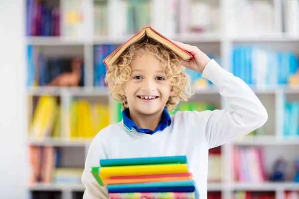 孩子们看书 孩子们读书 一个小男孩在一个五颜六色的书架上为学校做作业 学生与书籍 108 早期教育和发展 儿童之家图书馆 学龄前儿童学习 — 图库照片