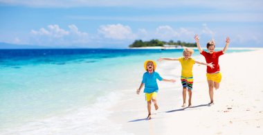 Tropik plajda oynayan çocuklar. Çocuklar yaz tatilinde yüzer ve denizde oynarlar. Kum ve su eğlencesi, güneş koruması. Okyanus kıyısında koşan ve zıplayan küçük çocuk.