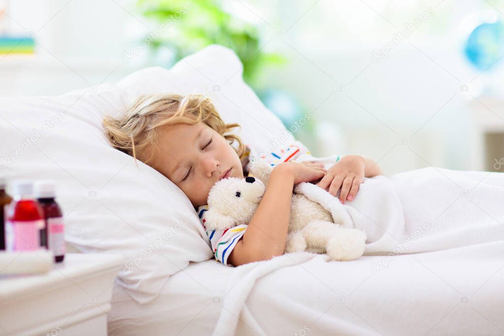 Sick little boy with asthma medicine. Ill child lying in bed. Unwell kid with chamber inhaler for cough treatment. Flu season. Bedroom or hospital room for young patient. Healthcare and medication.