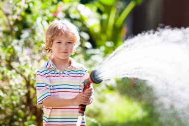 Bahçede çiçekleri ve bitkileri sulayan çocuk. Güneşli bahçesinde su hortumu olan bir çocuk. Küçük çocuk bahçeyle uğraşıyor. Evde yaz eğlencesi. Baharda aile aktivitesi. Çocuklar ebeveynlere yardım.