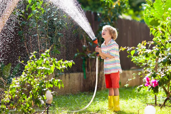 孩子们在花园里浇花浇花 在阳光灿烂的后院里带着水管的孩子 小男孩园艺 夏天在家里玩的很开心 春天的家庭活动 儿童帮助父母 — 图库照片