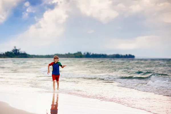 熱帯のビーチで遊んでいる子供たち 子供たちは夏休みに海で泳いだり遊んだりします 砂と水の楽しさ 太陽の保護 海の岸を走って飛び跳ねる小さな子供 — ストック写真