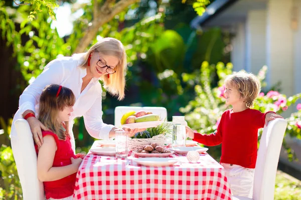 屋外で食べる家族 庭の夏の楽しみ 日当たりの良い裏庭でバーベキュー おばあちゃんと子供たちは屋外デッキで昼食を食べます 両親や子供たちはBbqをお楽しみください 男の子と女の子とともにお母さん — ストック写真