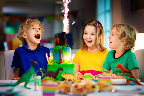 子供の誕生日パーティー 恐竜のテーマケーキ 小さな女の子がろうそくを吹いて贈り物を開く 子供向けイベント 恐竜をテーマにしたお祝いの装飾 — ストック写真