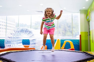 Çocuk renkli trambolinde atlıyor. Çocuklar anaokulundaki doğum günü partisinde şişme şatoya atlayıp küçük çocuklar için oyun merkezine giriyorlar. Küçük kız içeride oynuyor..