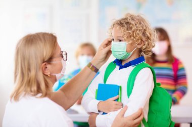 Sınıfta öğretmen, Corona virüsü ve grip salgını sırasında maskeli okul çocuğu. Erkek ve kız covid-19 karantina ve tecritten sonra okula dönüyorlar. Koronavirüsü önlemek için maskeli bir grup çocuk..