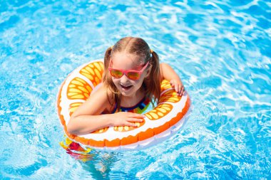 Yüzme havuzunda yüzen bir çocuk. Çocuklar yüzer. Küçük çocuklar için renkli sarı yüzer. Küçük kız yaz tatilinde tropikal tatil köyünde eğleniyor. Plaj ve su oyuncakları. Güneş koruması.