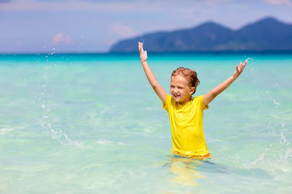 熱帯のビーチで遊んでいる子供たち 子供たちは夏休みに海で泳いだり遊んだりします 砂と水の楽しさ 幼い子供のための太陽の保護 海の岸を走って飛び跳ねる少年 — ストック写真