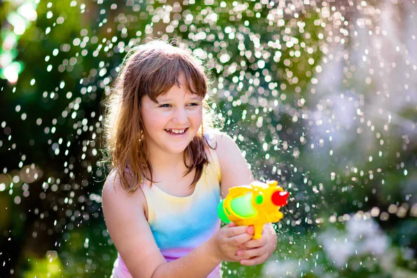 Kids play with water gun toy in garden. Outdoor summer fun. Little boy playing with water hose in sunny backyard. Party game for children. Healthy activity for hot sunny day.