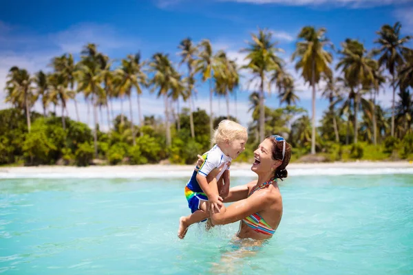 ヤシの木と熱帯のビーチで母親と赤ちゃん 母親と小さな男の子が水泳や水で遊んでいます エキゾチックな島で家族の夏休み 子供と一緒に旅行する 太陽の保護と水着 — ストック写真