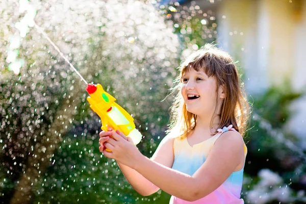 子供たちは庭で水銃のおもちゃで遊ぶ 屋外の夏の楽しみ 日当たりの良い裏庭で水のホースで遊んでいる小さな男の子 子供のためのパーティーゲーム 暑い晴れた日のための健康的な活動 — ストック写真