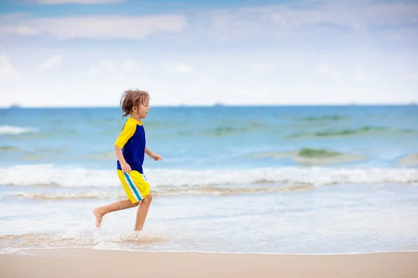 熱帯のビーチで遊んでいる子供たち 子供たちは夏休みに海で泳いだり遊んだりします 砂と水の楽しさ 太陽の保護 海の岸を走って飛び跳ねる小さな子供 — ストック写真