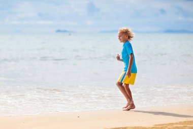 Tropik plajda oynayan çocuklar. Çocuklar yaz tatilinde yüzer ve denizde oynarlar. Kum ve su eğlencesi, küçük çocuklar için güneş koruması. Okyanus kıyısında koşan ve zıplayan küçük çocuk.