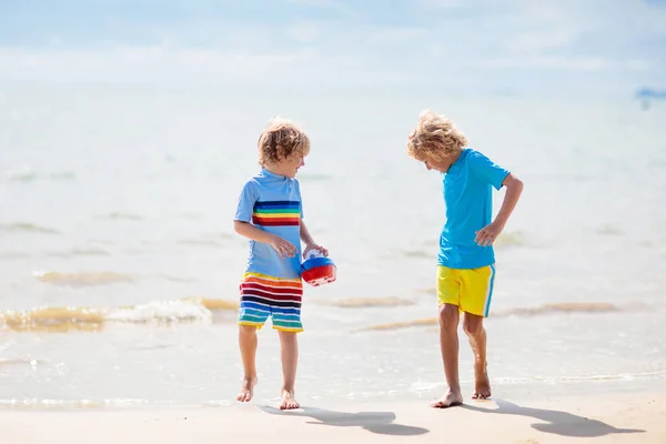 熱帯のビーチで遊んでいる子供たち 子供たちは夏休みに海で泳いだり遊んだりします 砂と水の楽しさ 幼い子供のための太陽の保護 海の岸を走って飛び跳ねる少年 — ストック写真