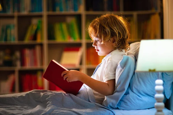 孩子在床上看书 孩子们晚上看书 小男孩儿卧室里有童话故事书幼儿的教育 晚上睡前讲故事 可爱的孩子在黑暗的房间与灯的毛毯下 — 图库照片