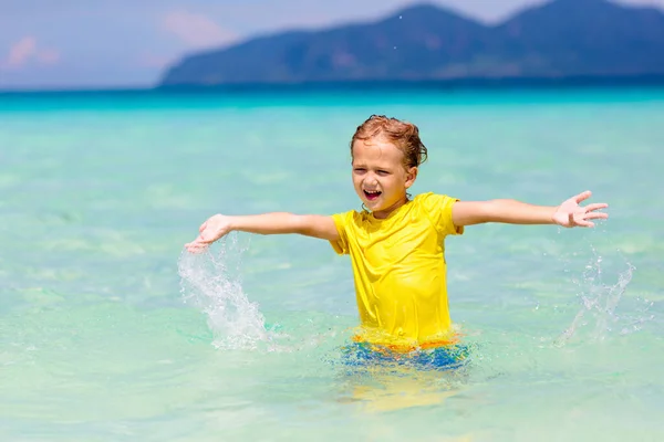 熱帯のビーチで遊んでいる子供たち 子供たちは夏休みに海で泳いだり遊んだりします 砂と水の楽しさ 幼い子供のための太陽の保護 海の岸を走って飛び跳ねる少年 — ストック写真