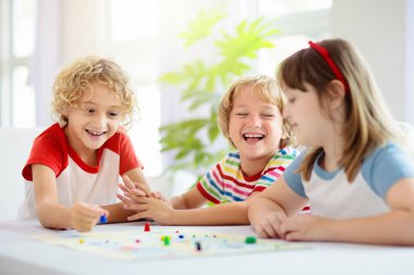 Aile evde masa oyunu oynuyor. Çocuklar stratejik oyunlar oynar. Küçük çocuk zar atıyor. Yaz tatili için eğlenceli bir ev aktivitesi. Kardeşler arası bağ. Eğitici oyuncaklar. Arkadaşlar oyun gecesinin tadını çıkarın.