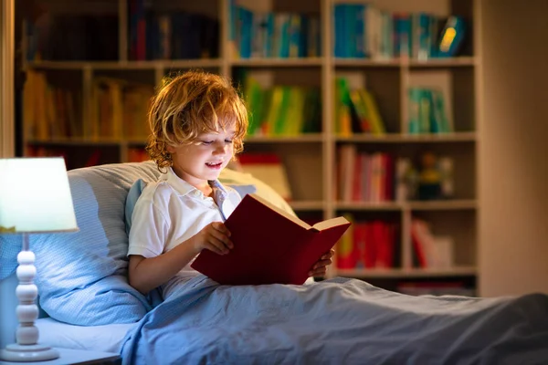 孩子在床上看书 孩子们晚上看书 小男孩儿卧室里有童话故事书幼儿的教育 晚上睡前讲故事 可爱的孩子在黑暗的房间与灯的毛毯下 — 图库照片