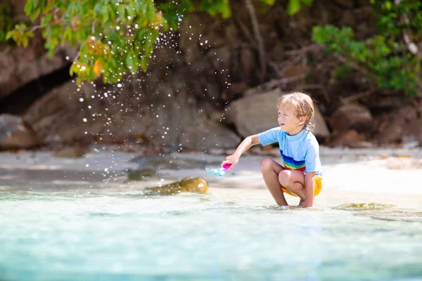 熱帯のビーチで遊んでいる子供たち 水のスプラッシュ楽しい 小さな男の子の海の波の中で水しぶき 子供たちは夏休みに泳いだり遊んだりします 砂と水のおもちゃ 幼い子供のための太陽の保護 — ストック写真