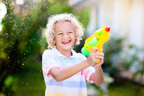 子供たちは庭で水銃のおもちゃで遊ぶ 屋外の夏の楽しみ 日当たりの良い裏庭で水のホースで遊んでいる小さな男の子 子供のためのパーティーゲーム 暑い晴れた日のための健康的な活動 — ストック写真