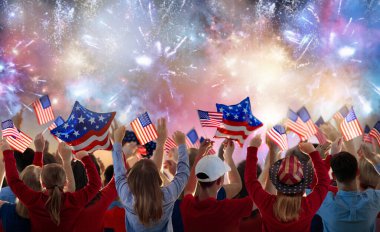 Amerikan ailesi 4 Temmuz 'u kutluyor. Independence Day havai fişeklerini izleyen insanlar Amerikan bayrağı taşıyor. Gururlu ABD kalabalığı tezahürat ve kutlama yapıyor. Amerikan sembollü bir grup. Ulusal bayram partisi.