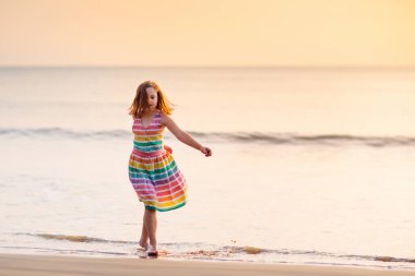 Okyanus sahilinde oynayan bir çocuk. Gün batımında dalgalara atlayan bir çocuk. Çocuklu aileler için deniz tatili. Yaz tatili boyunca egzotik adanın tropik sahillerinde koşan güzel elbiseli küçük kız..