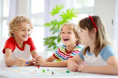 Aile evde masa oyunu oynuyor. Çocuklar stratejik oyunlar oynar. Küçük çocuk zar atıyor. Yaz tatili için eğlenceli bir ev aktivitesi. Kardeşler arası bağ. Eğitici oyuncaklar. Arkadaşlar oyun gecesinin tadını çıkarın.