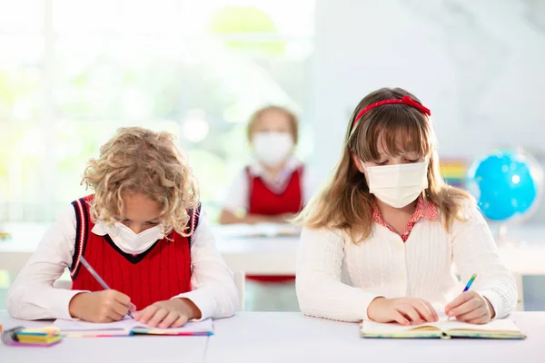 Kids in face mask in school class. Child back to school after coronavirus lockdown. Primary child in covid-19 pandemic. Safety and virus spread prevention. Student in surgical mask. Social distancing.