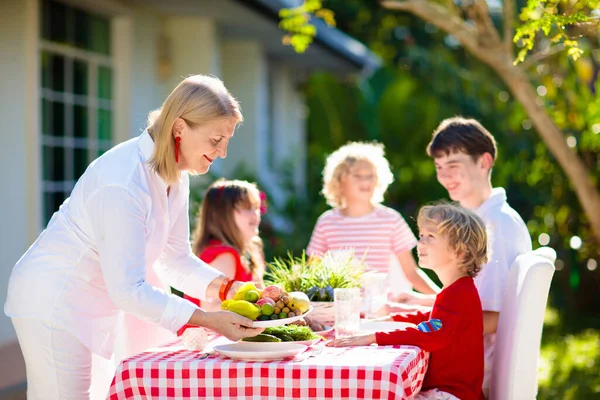 屋外で食べる家族 庭の夏の楽しみ 日当たりの良い裏庭でバーベキュー おばあちゃんと子供たちは屋外デッキで昼食を食べます 両親や子供たちはBbqをお楽しみください 男の子と女の子とともにお母さん — ストック写真