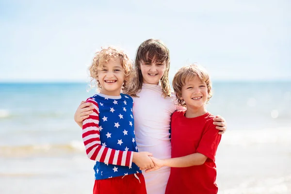 Kids run with USA flag on sunny beach. 4th of July celebration. American family fun on Independence Day weekend. Patriotic children celebrate US holiday. Boy and girl with symbols of America.