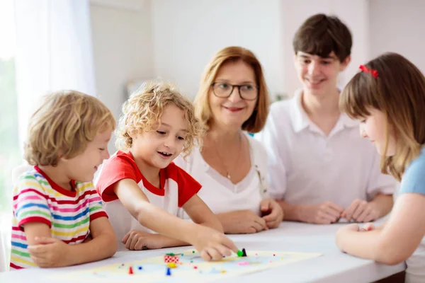 Family playing board game at home. Kids play strategic game. Little boy throwing dice. Fun indoor activity for summer vacation. Siblings bond. Educational toys. Friends enjoy game night.